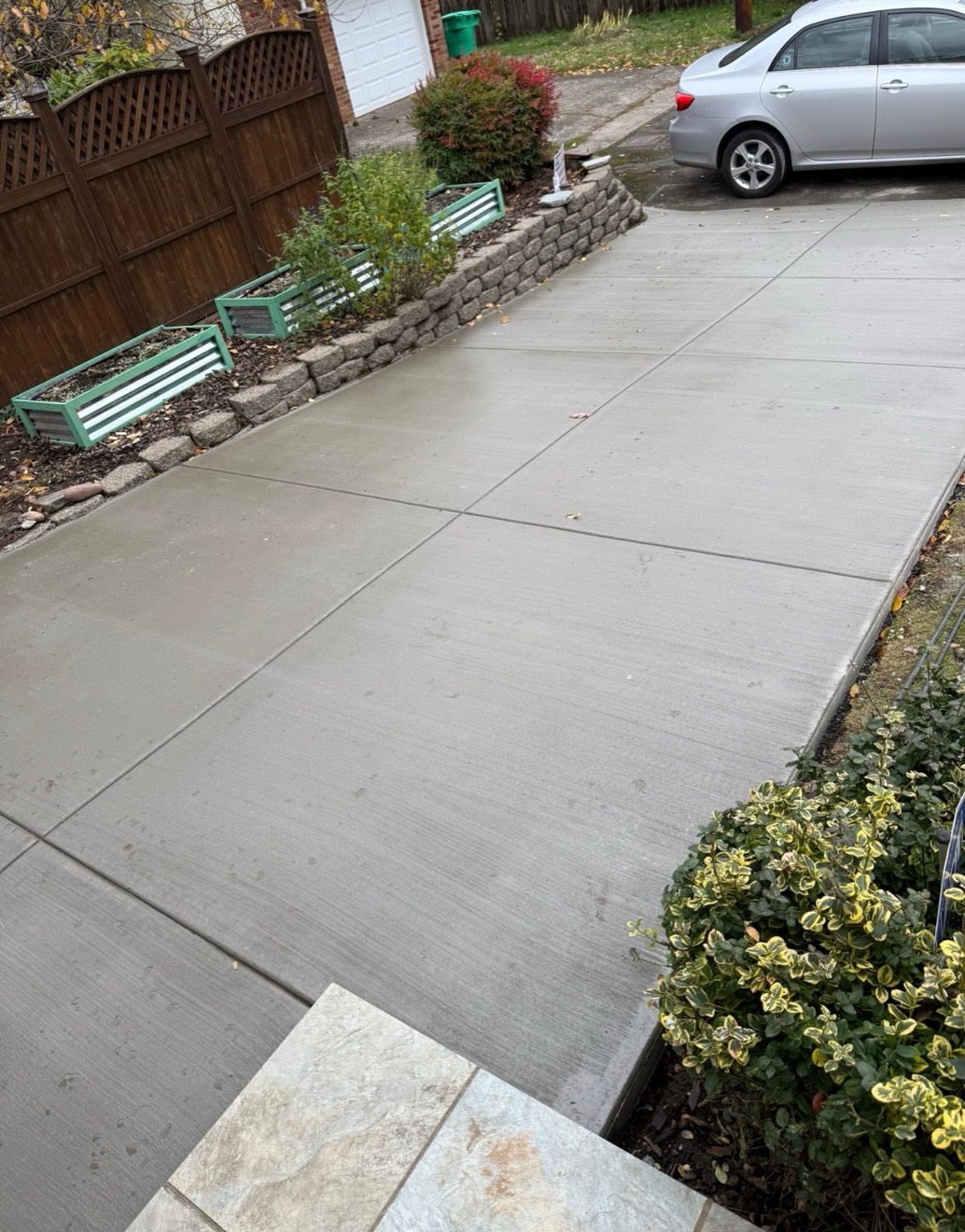 Narrow concrete driveway bordered by a fence and stone garden walls